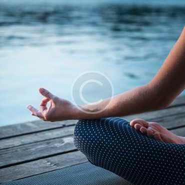 Meditating by the lake, sitting in lotus position, relaxed, selective focus